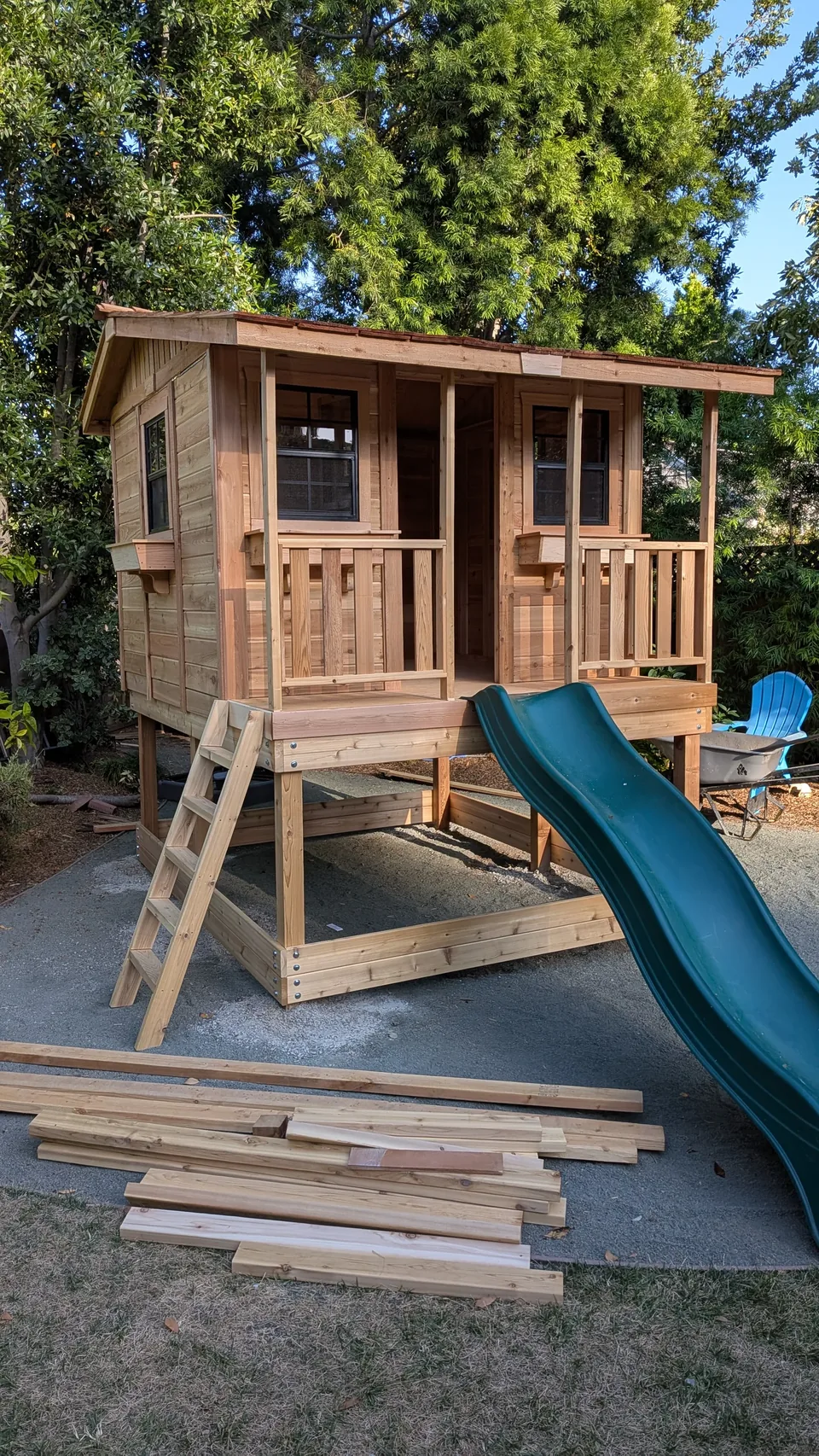 Raised wooden playhouse with porch railing, ladder, and green slide, assembled by Artem in May 2026